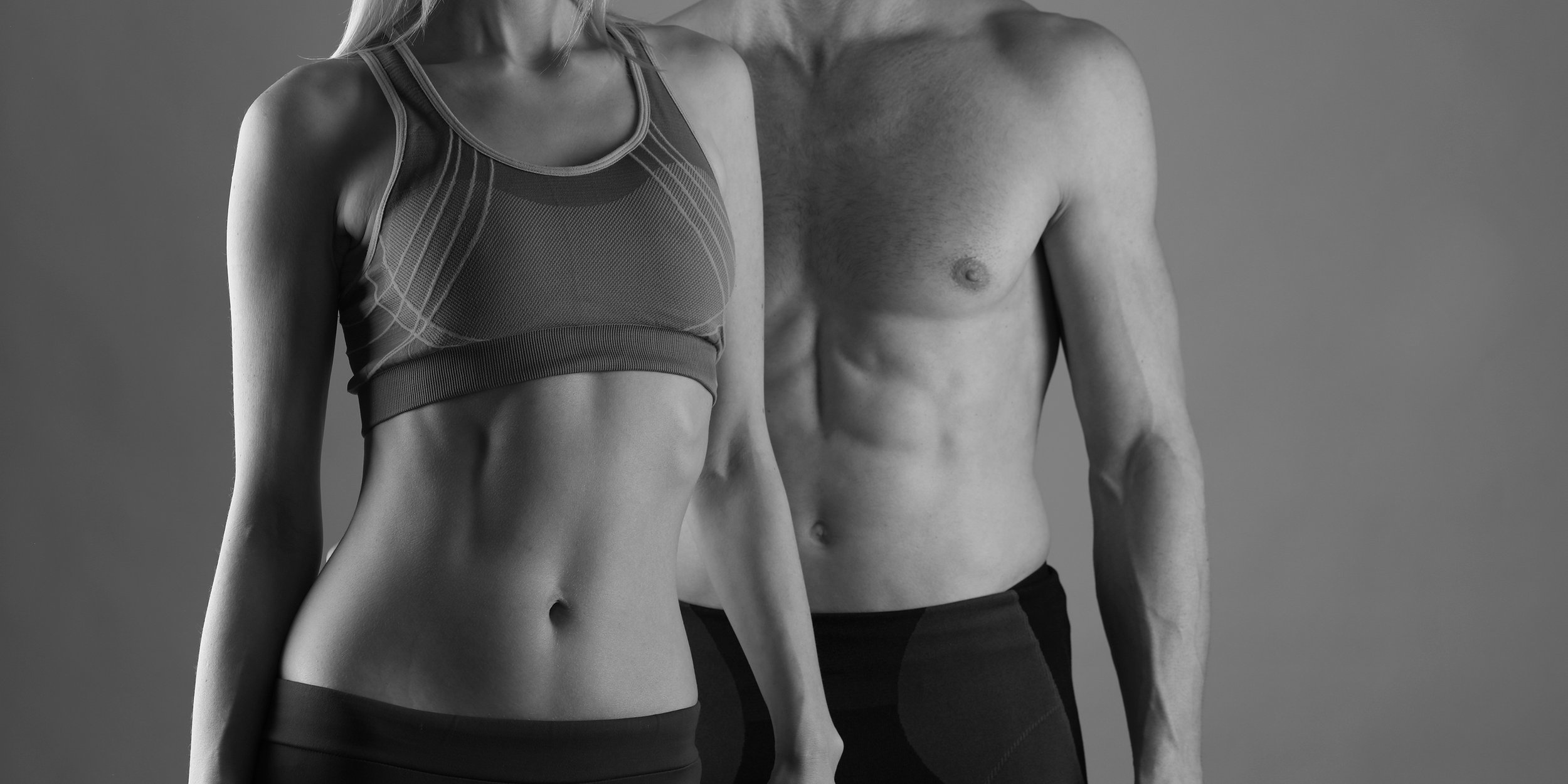 Black and white photo of a fit woman in a sports bra and a fit man shirtless, both showing toned bodies from the waist up.