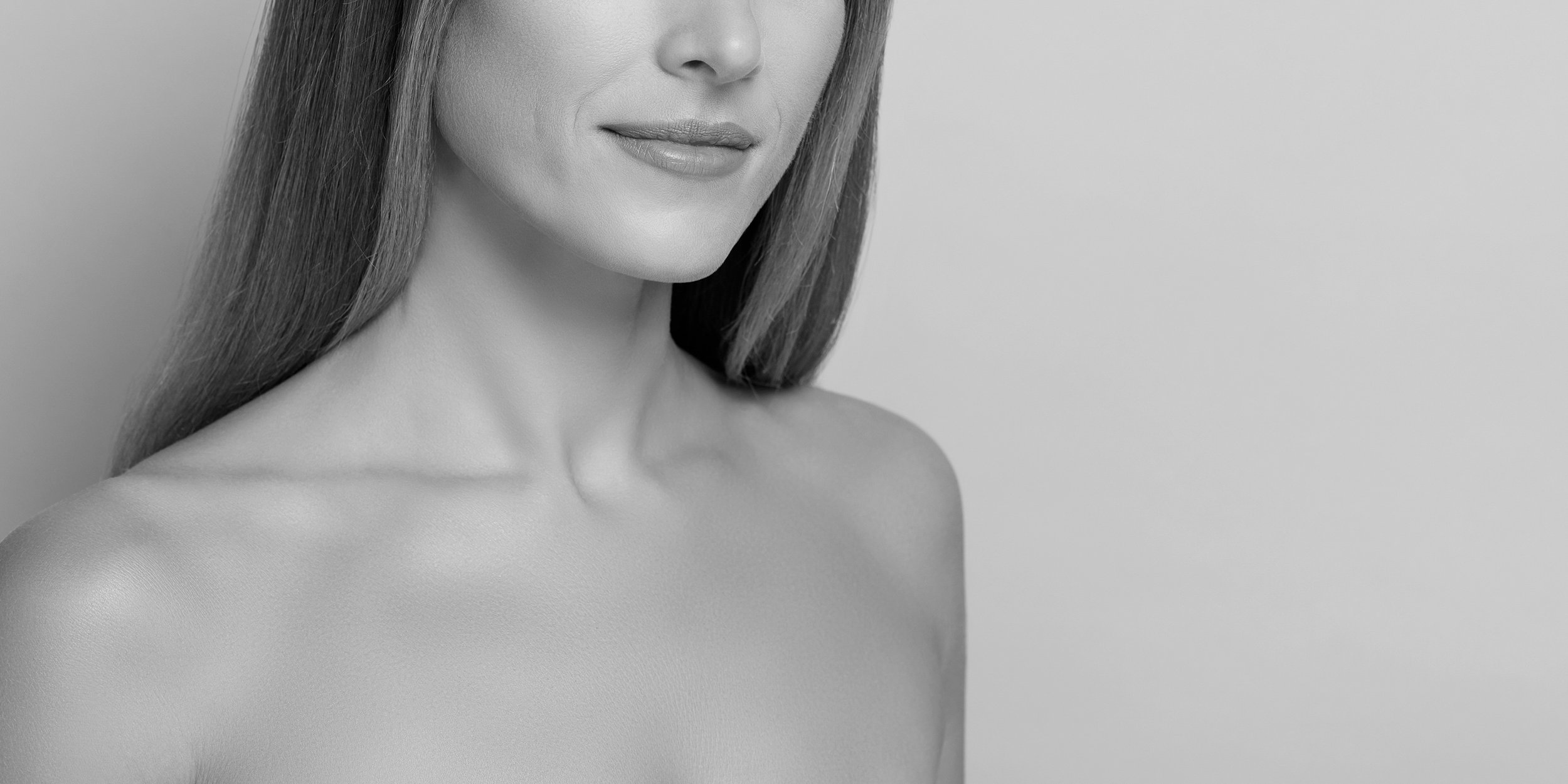 Black and white close-up photo of a woman with smooth skin, smiling lips, and long hair, cropped at the shoulders.
