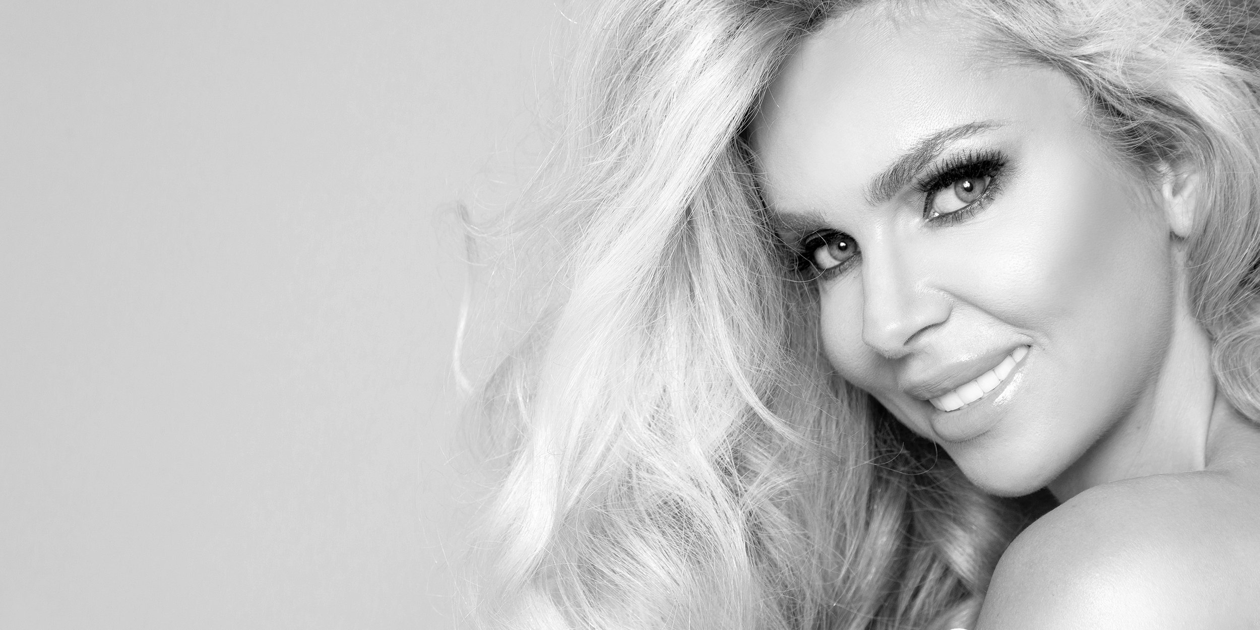 Close-up black and white photograph of a smiling woman with long, wavy hair and bright eyes.