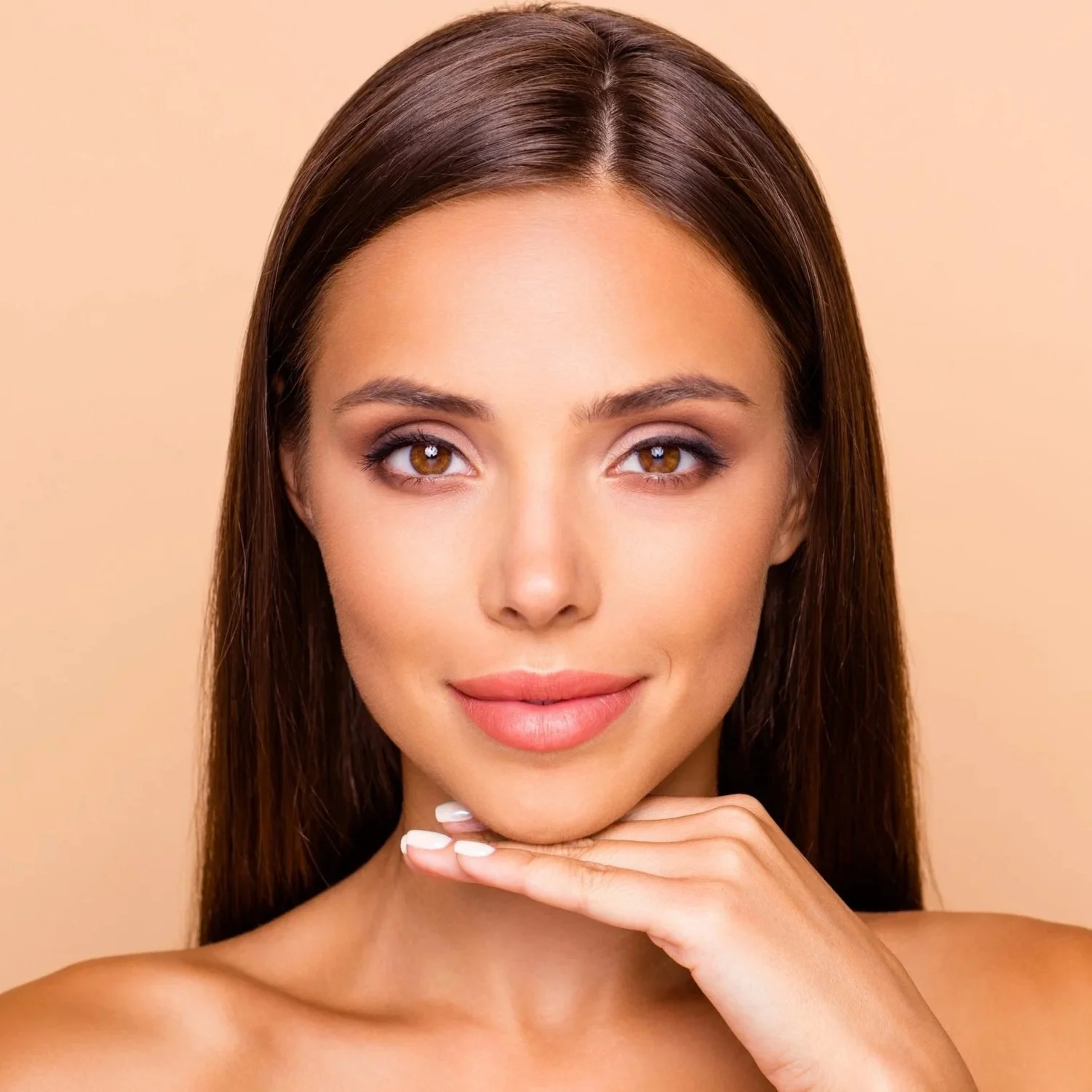 Close-up of a woman with brown hair and makeup, resting her chin on her hand against a beige background.