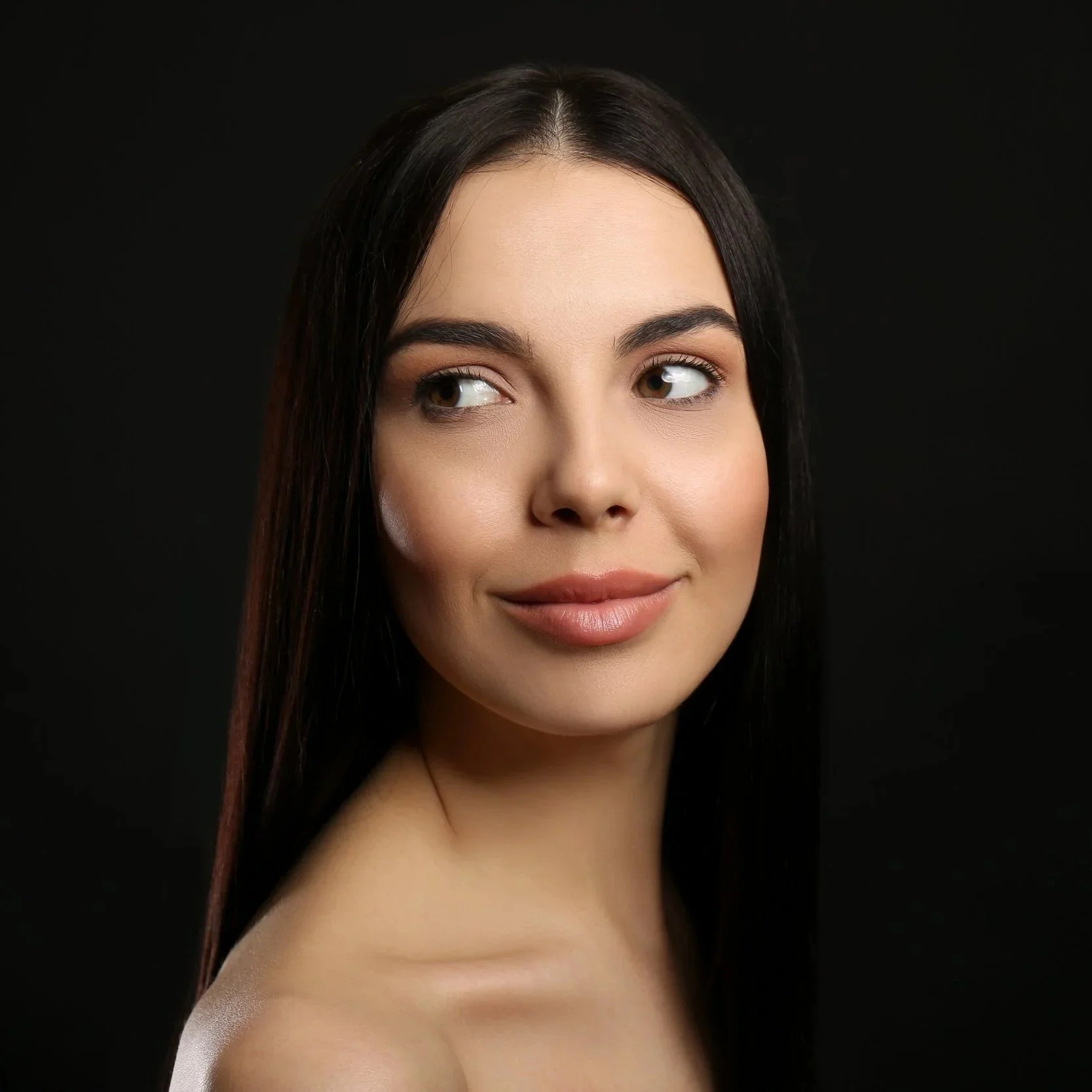 Close-up portrait of a young woman with long dark hair, looking to the side, with a neutral expression, against a black background.
