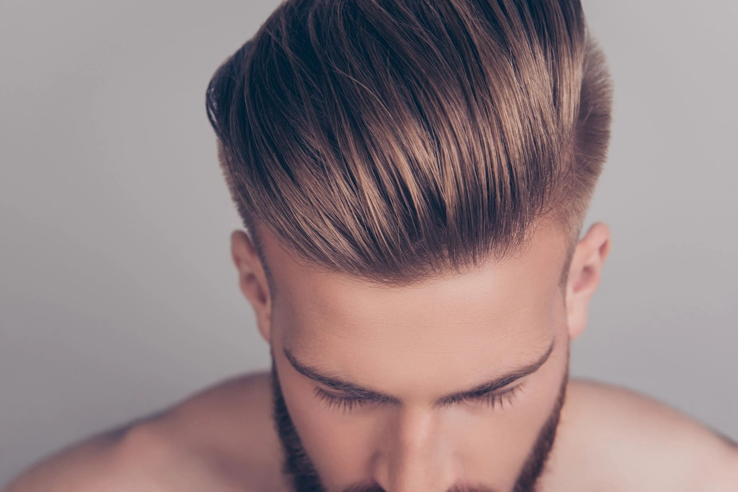 Close-up of a man's hairstyle with voluminous, neatly styled hair and a beard, looking downward.