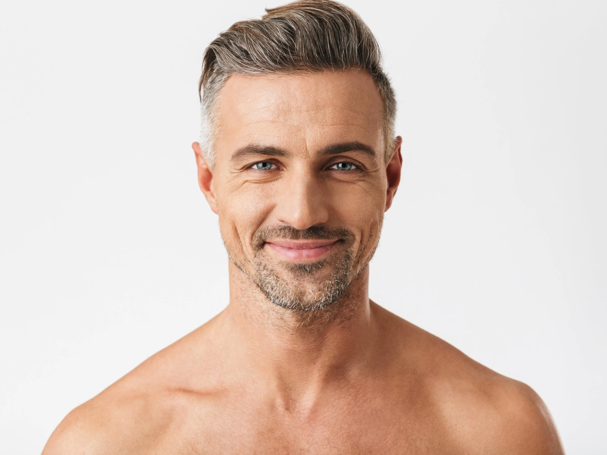 Close-up of a middle-aged man with short, graying hair and a trimmed beard, smiling at the camera with no shirt, against a plain white background.