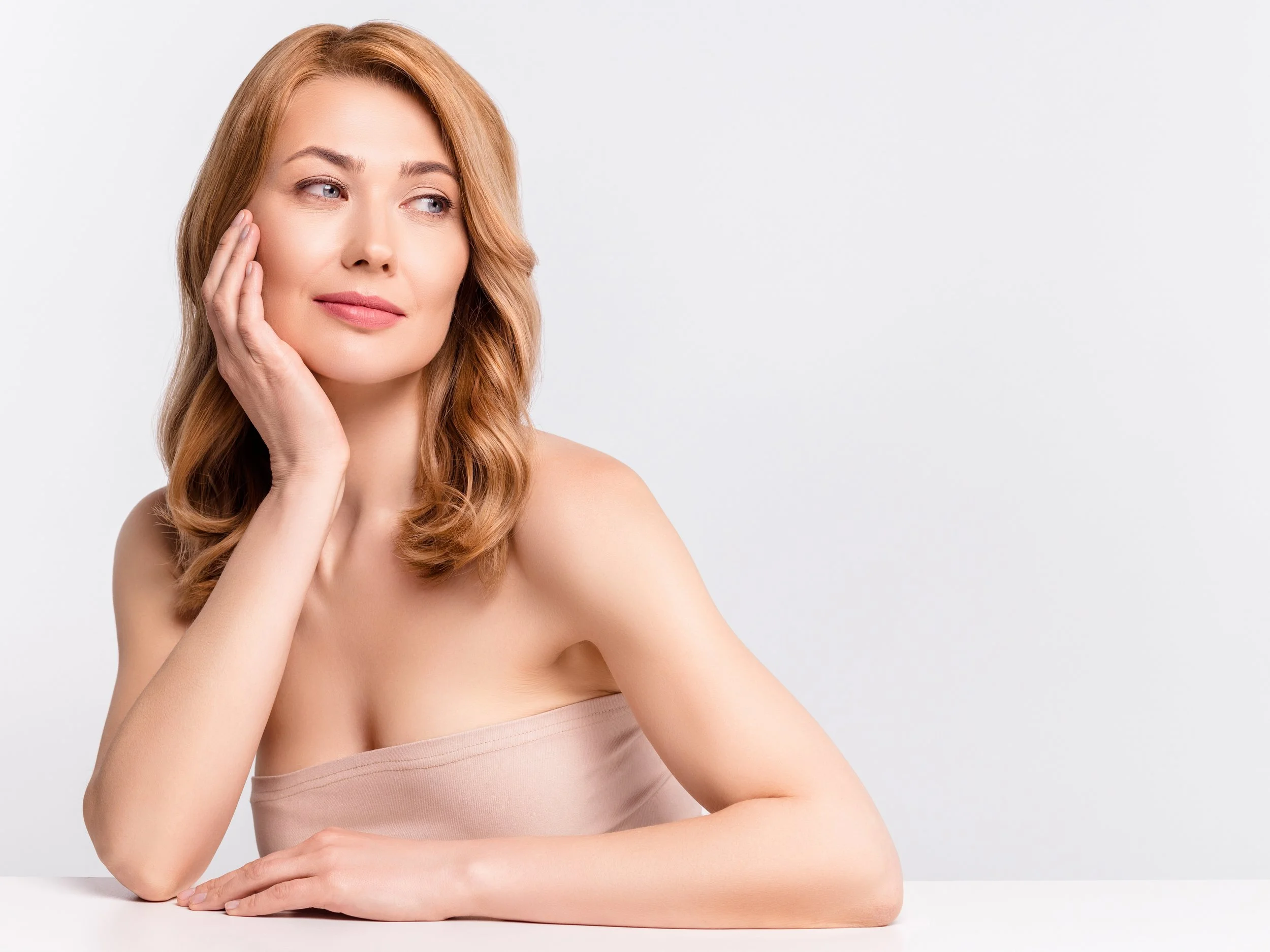 A woman with shoulder-length reddish-brown hair, resting her chin on her left hand with a thoughtful expression, against a plain white background.
